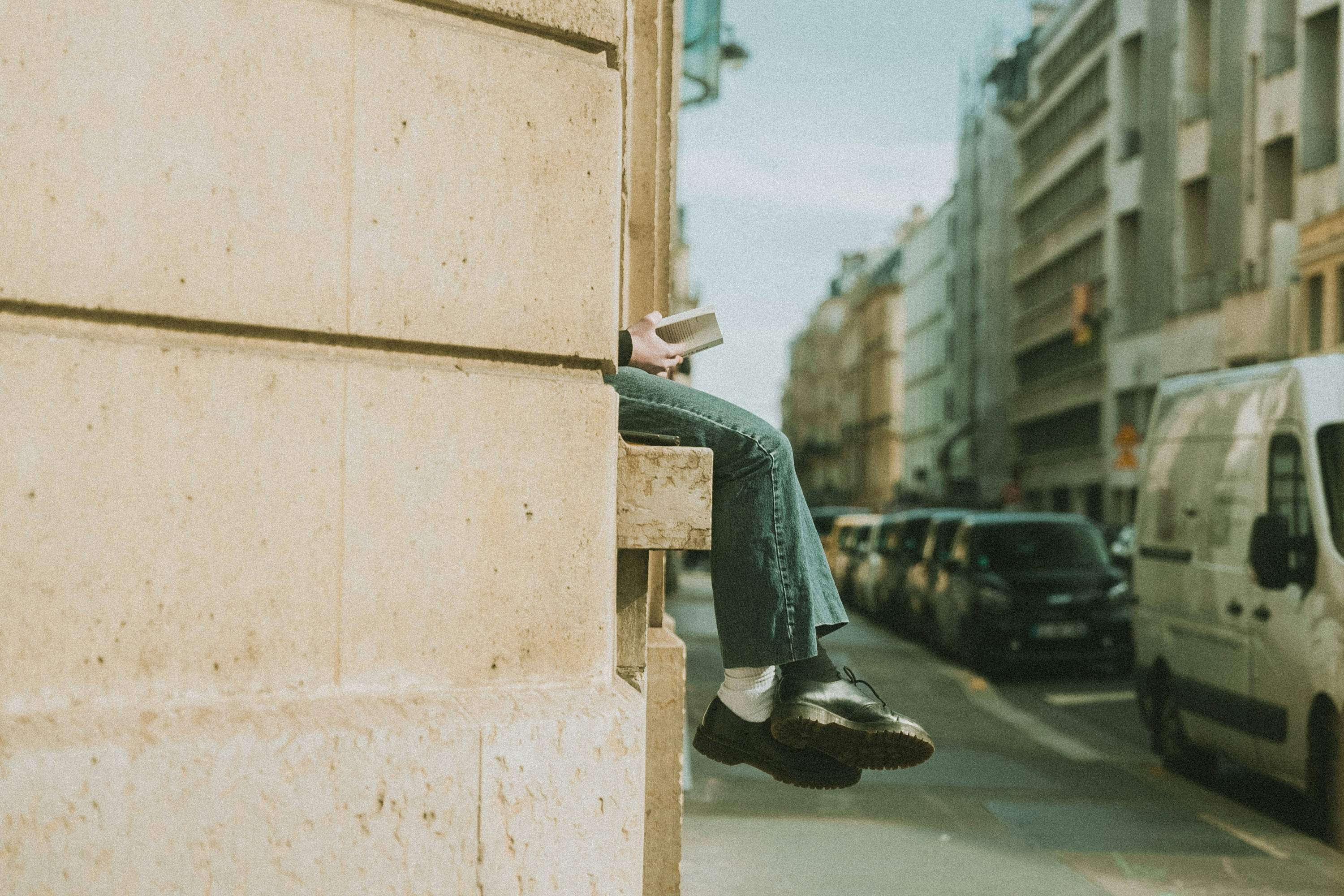 A person sitting on a stone ledge with a book